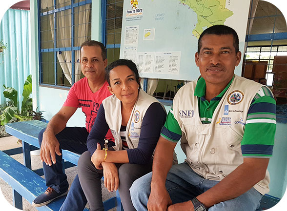 Dos hombres y una mujer, sentados en una banca sonriendo. 
