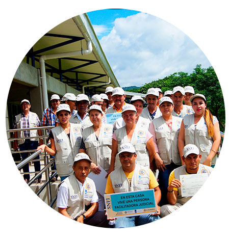 Varias personas, hombre sostiene rótulo que dice: en esta casa vive una persona Facilitadora Judicial