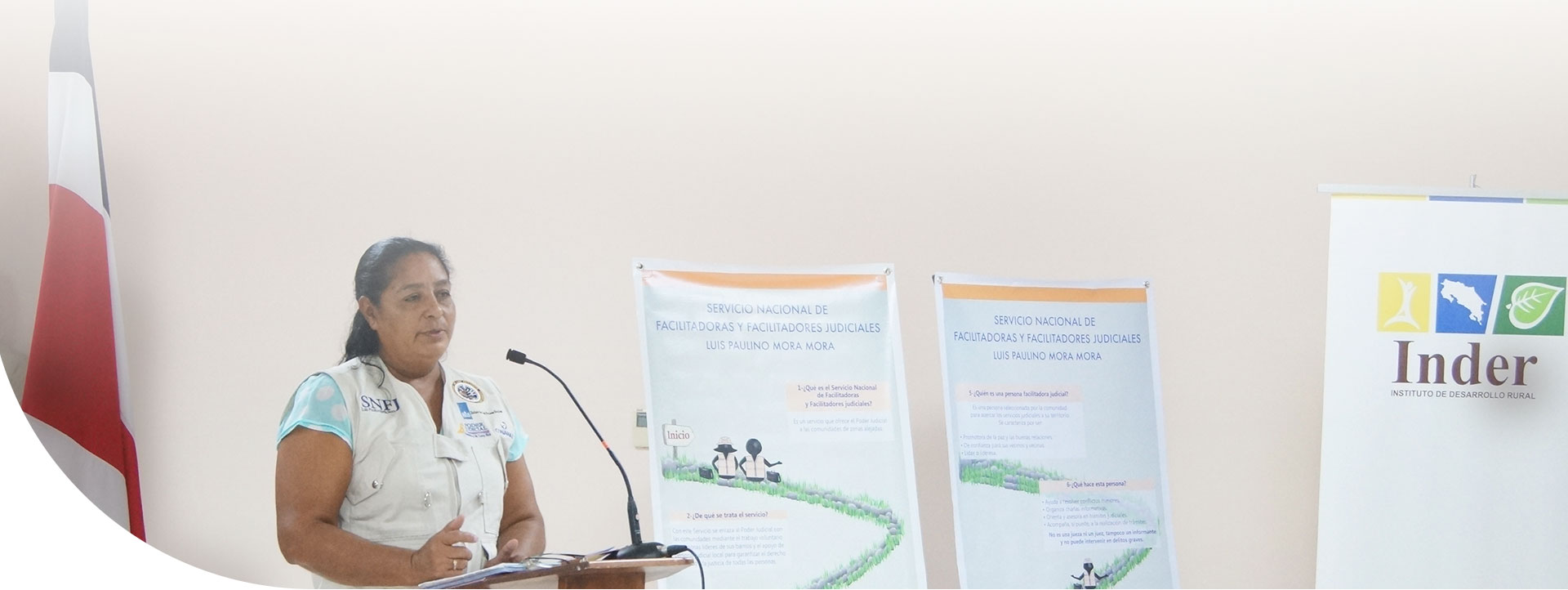 mujer hablando en un podio, atrás está la bandera de Costa Rica y dos banners